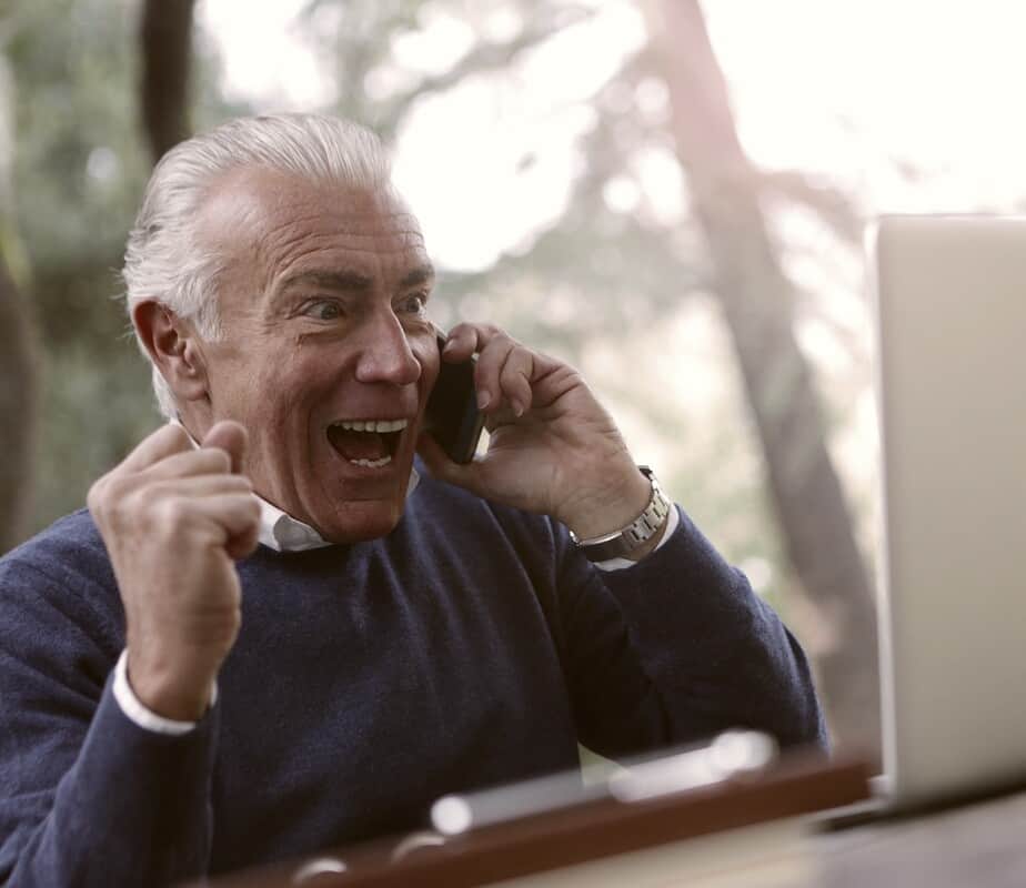 Excited man on a phone, sitting in front of a laptop